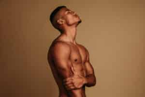 Man with sculpted abs poses in side profile after Emsculpt NEO® treatment